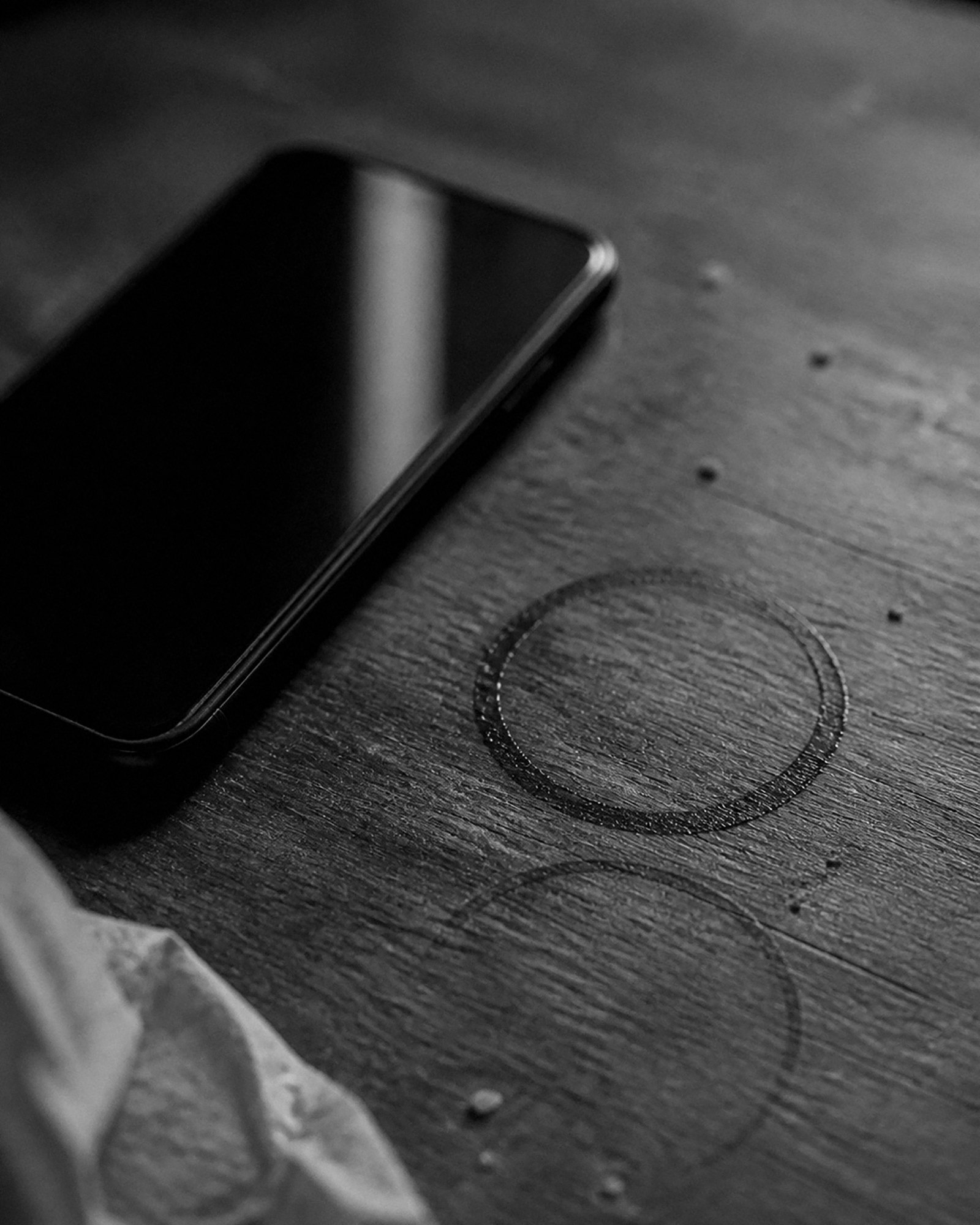 Detalle de una mesa de madera con un teléfono apagado y dos marcas secas de vaso sobre la madera.